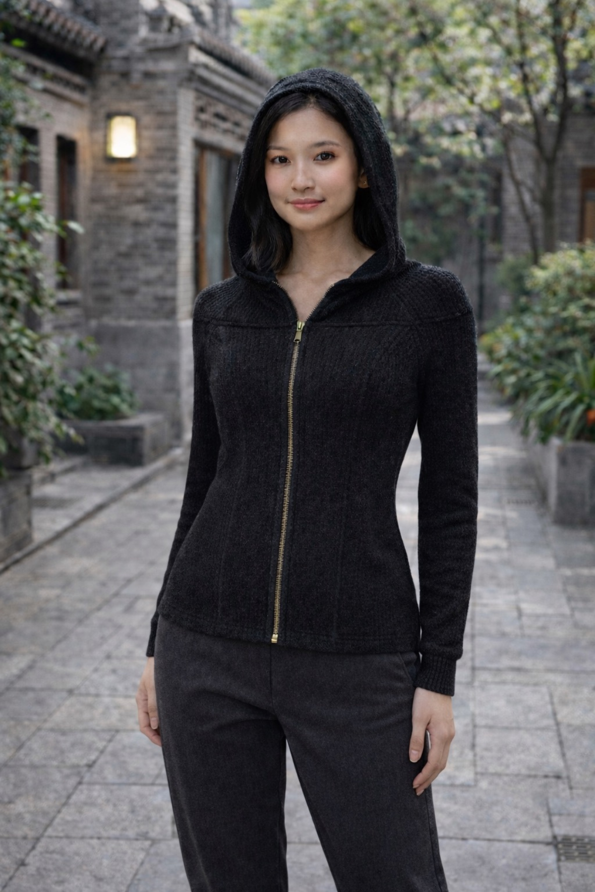Woman wearing black knitted convertible hoodie travel outfit  and pants standing in an outdoor setting with traditional architecture