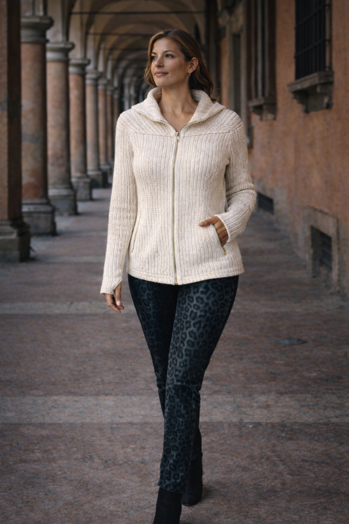 Woman wearing a white convertible travel hoodie and chic cargo pants walking in an outdoor setting with arches