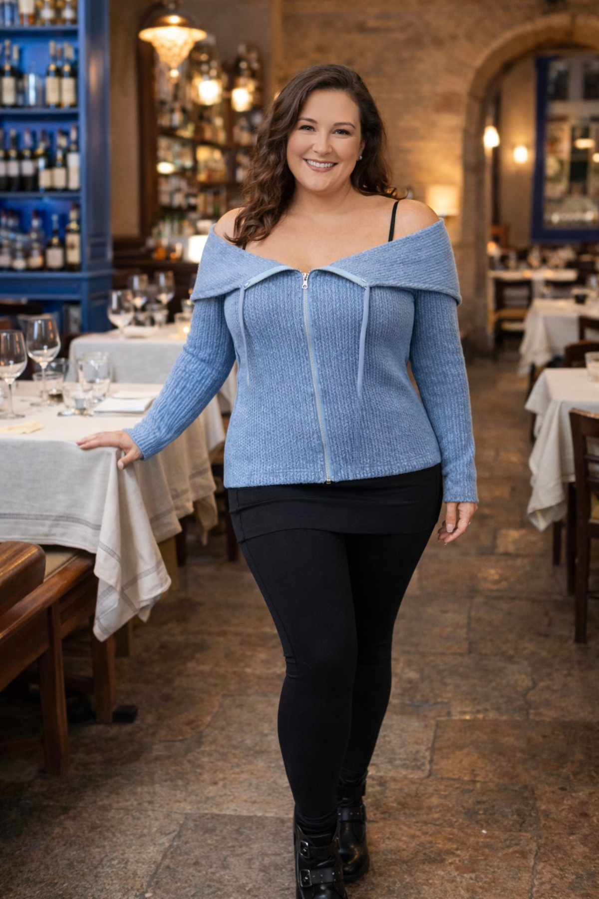 A woman standing and wearing a blue knitted convertible hoodie travel outfit