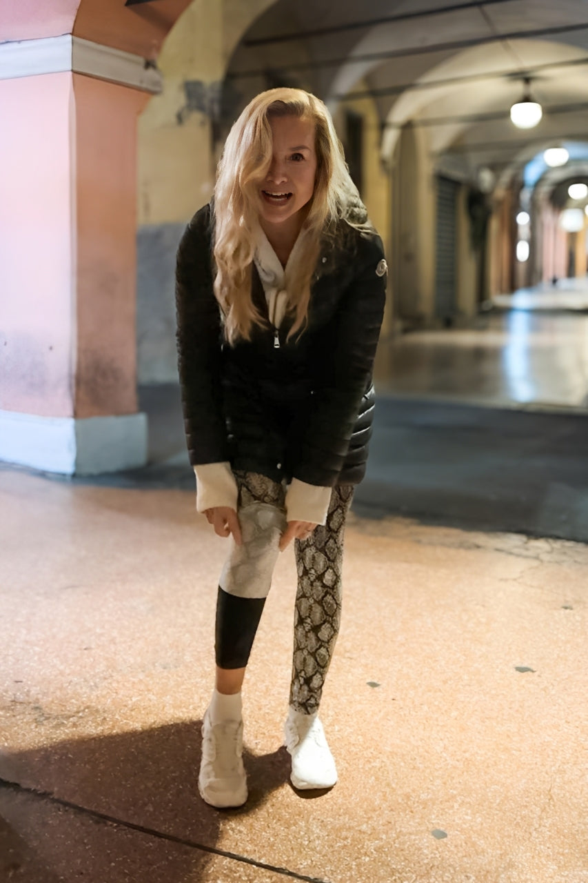 Diane Kroe in black jacket and travel tights showing the new Travel Leg Warmer standing in a tunnel-like setting